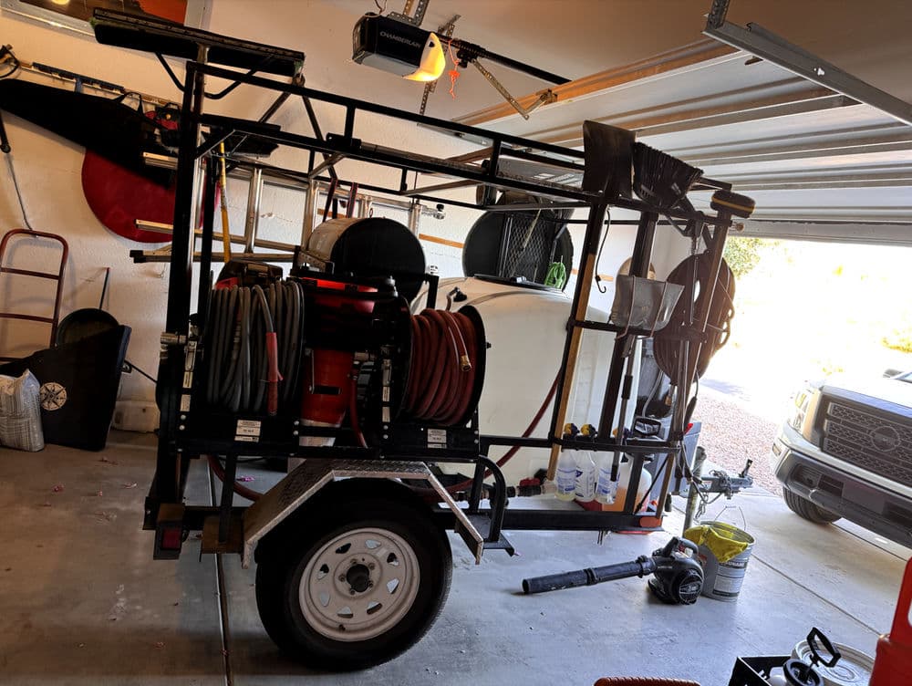 Utility trailer with equipment and hoses organized, parked in a garage.