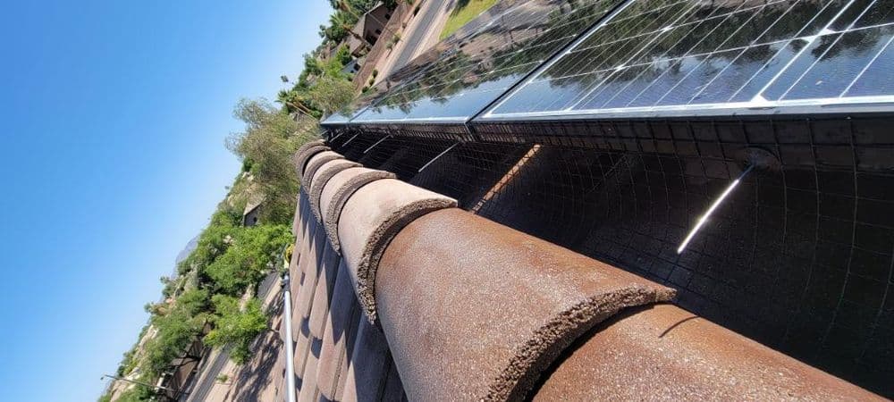 Rooftop view with solar panels and a corrugated pipe under clear blue sky.
