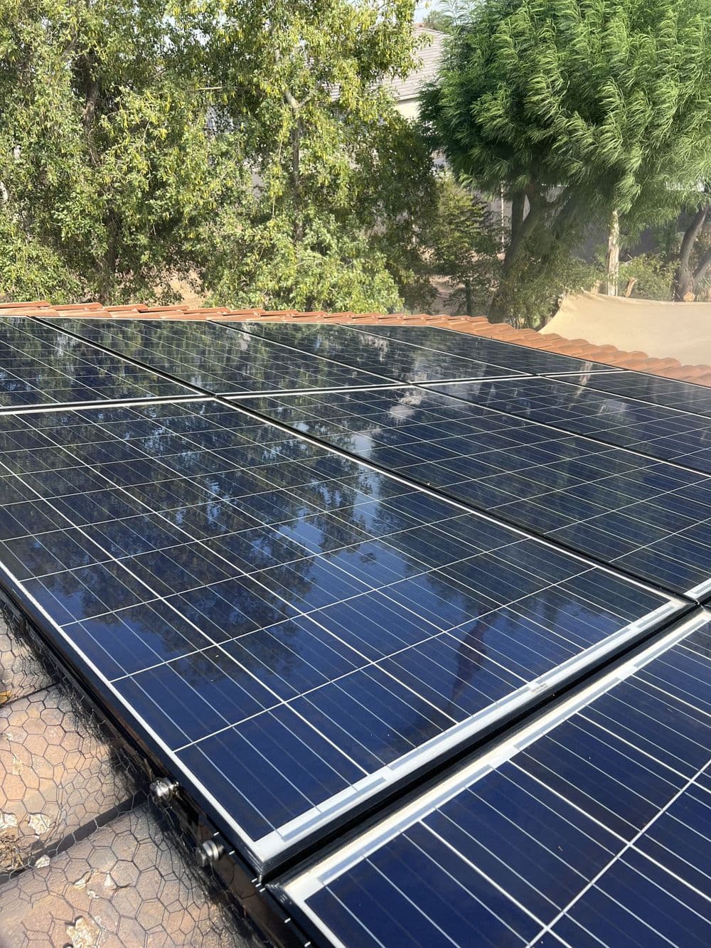 Solar panels installed on a roof with trees in the background, capturing sunlight.